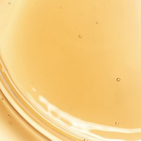 Close-up of a smooth golden serum texture with visible moisture droplets on a clear surface