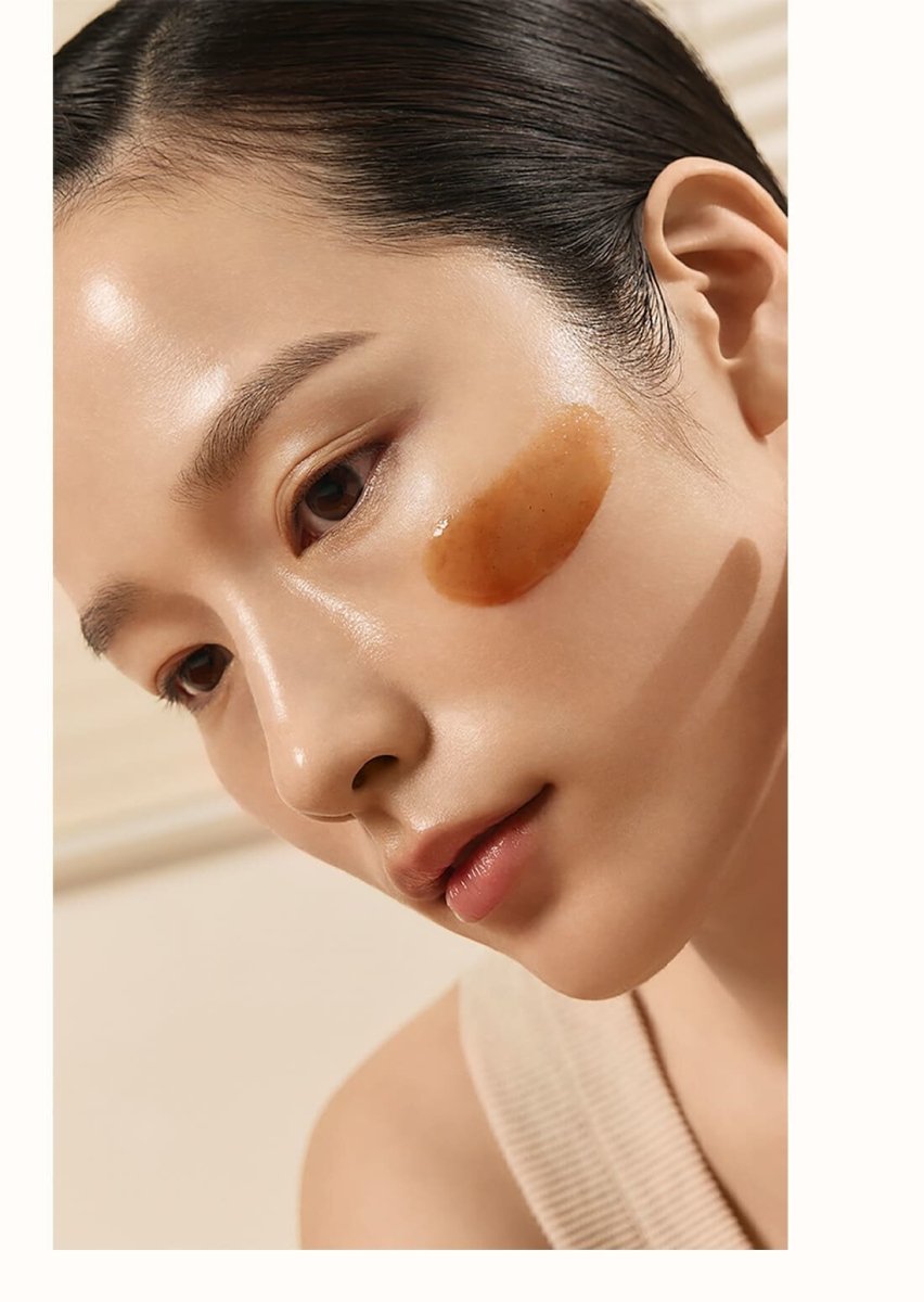 Close-up of a woman with smooth skin applying a warm-toned clarifying mask on her cheek for a glowing complexion