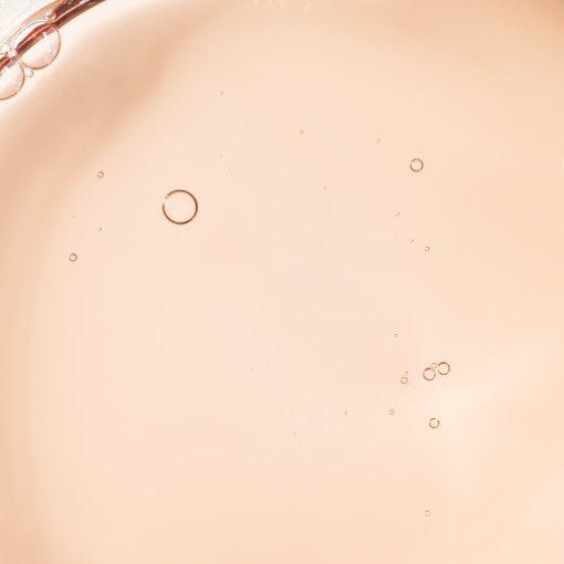 Close-up of a pale peach rejuvenating ampoule liquid with small air bubbles suspended in it