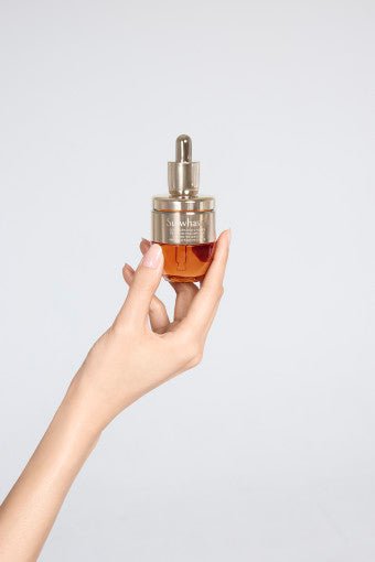 Hand holding amber glass dropper bottle of rejuvenating ampoule with gold metallic cap on light background