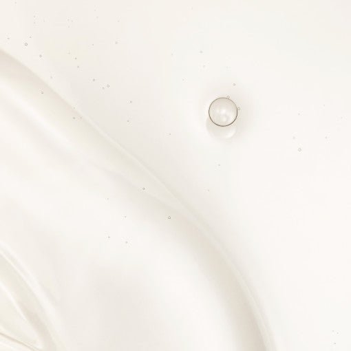 Droplet of clear rejuvenating water with tiny bubbles suspended in smooth, translucent liquid texture on white surface