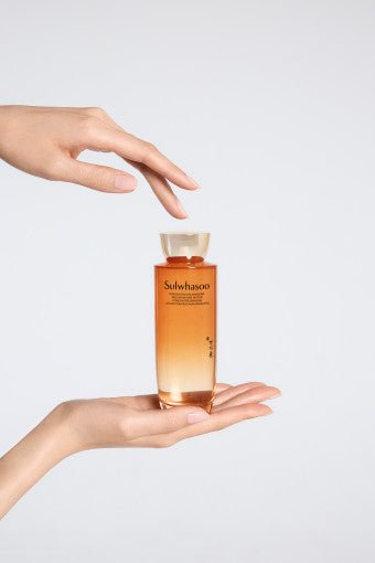 Transparent amber bottle of rejuvenating essence held delicately between hands on clean white background