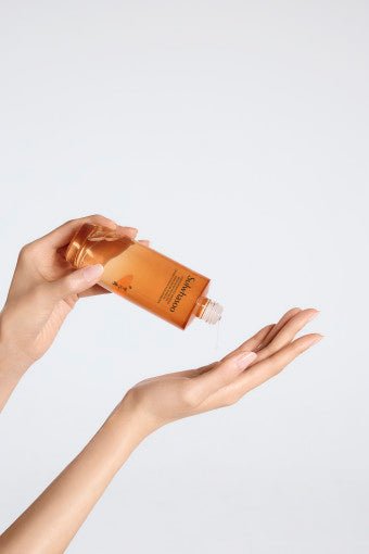 Hand pouring amber-toned rejuvenating water into palm, showcasing smooth skin and refined bottle design.