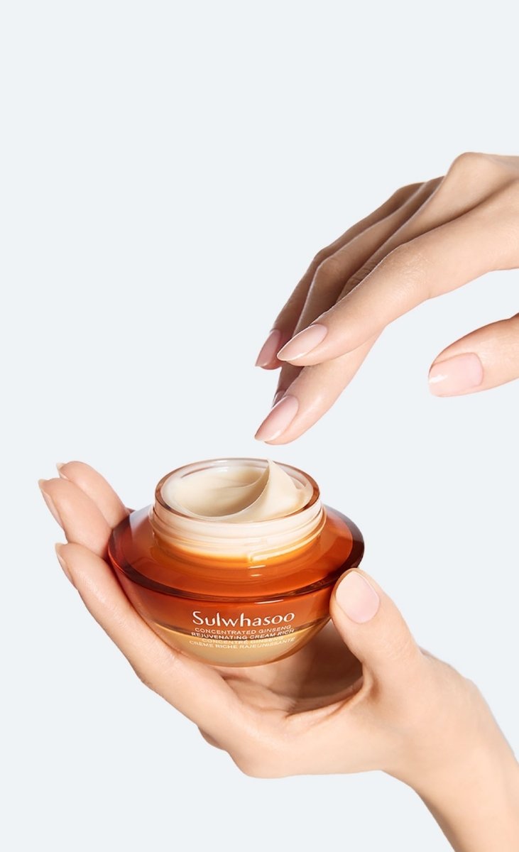 Hands holding an amber jar of rich anti-aging ginseng cream with a smooth creamy texture on pale background