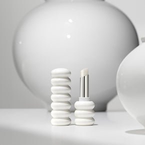 Minimalist white lip balm tube with raised ring design and smooth balm tip on neutral background