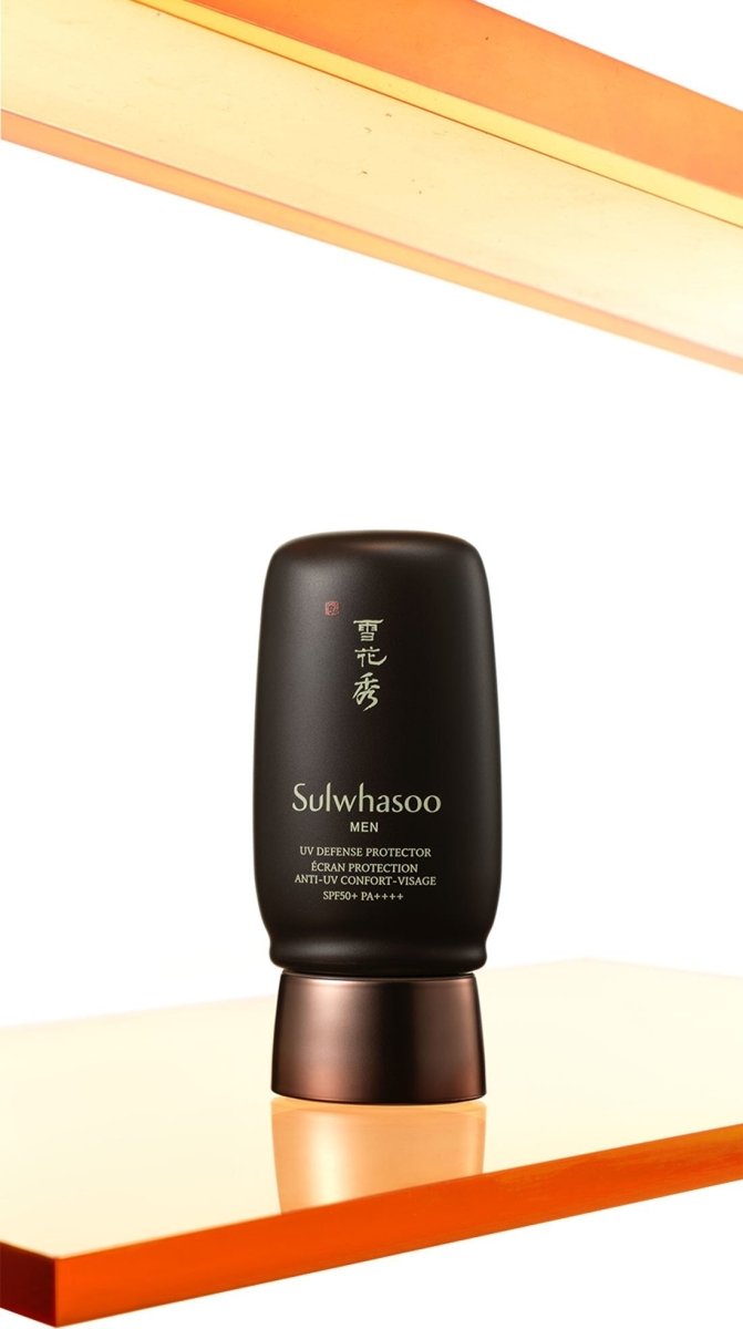 Matte black bottle of men’s UV defense protector with copper cap, shown on glossy amber surface with reflection