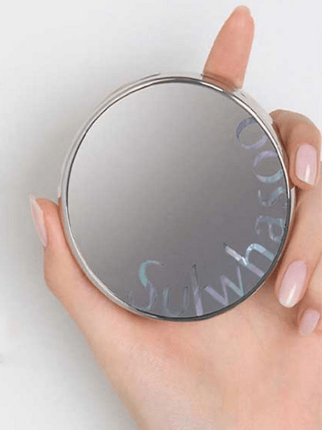 Hand holding a sleek silver compact cushion foundation case with iridescent brand lettering on top