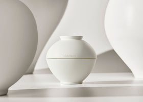 Minimalist round ivory cream jar with subtle brand embossing and smooth matte finish on soft beige background