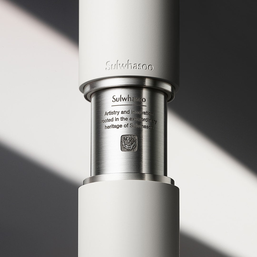 Close-up of sleek matte white and brushed metal serum bottle segment with engraved brand name and heritage text detail