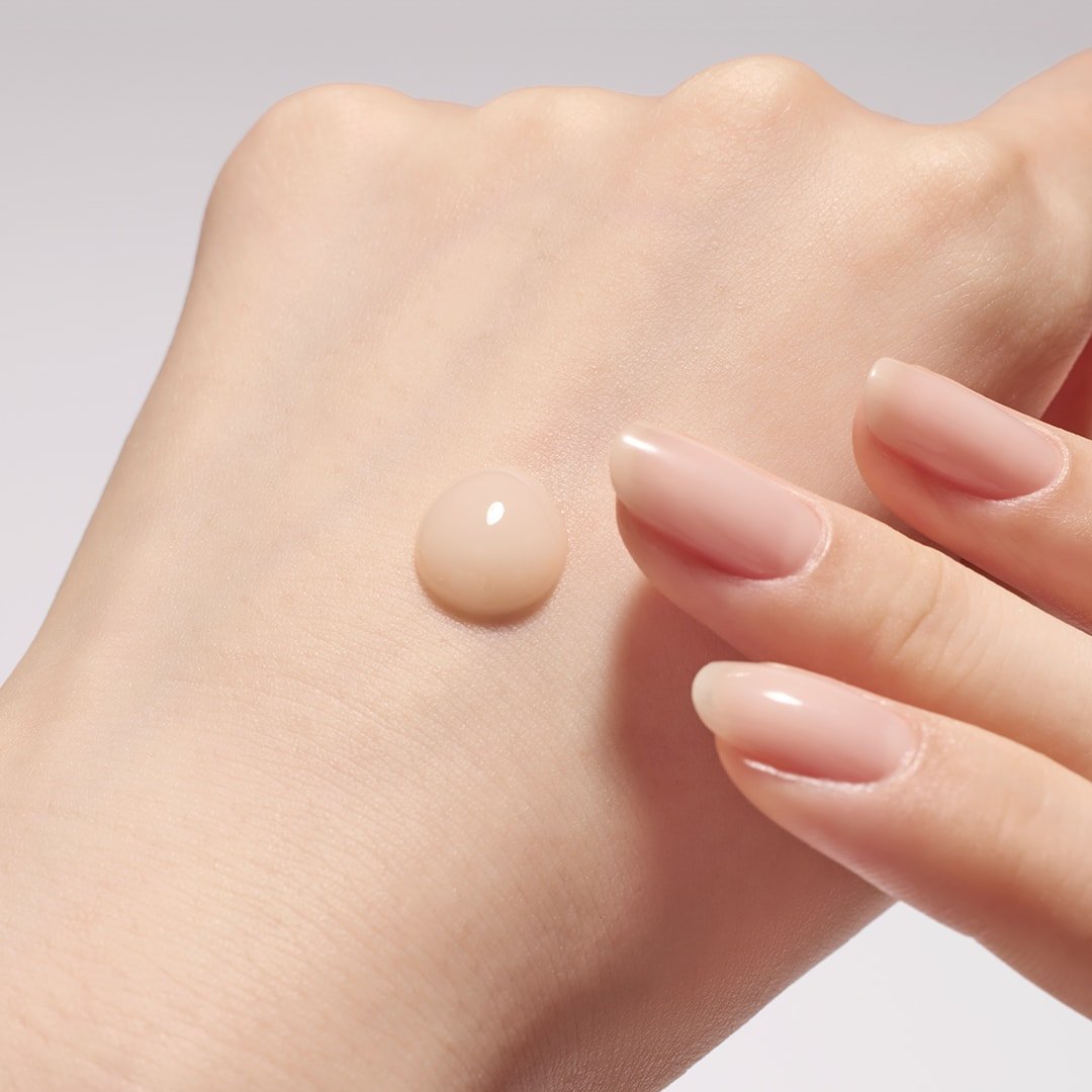 Light beige serum droplet on smooth skin with manicured nails poised to apply for a hydrated, even finish