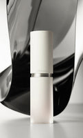 Minimalist frosted glass serum bottle with matte white cap against abstract black and gray reflective backdrop