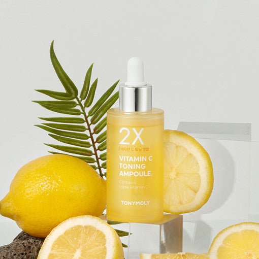 Frosted yellow dropper bottle of brightening vitamin C ampoule with fresh lemon slices and green leaf backdrop