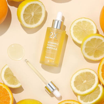 Clear dropper bottle of vitamin C serum surrounded by fresh lemon and orange slices on light background