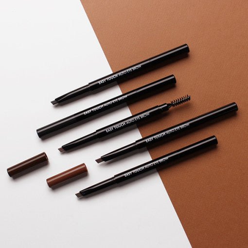 Four slim black eyebrow pencils with angled tips and spoolie brush, placed on brown and white background
