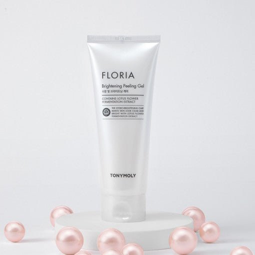 White tube of brightening peeling gel standing on white platform surrounded by soft pink pearl-like spheres