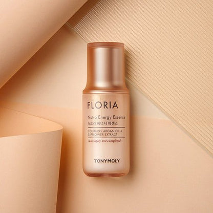 Matte peach-colored bottle of hydrating essence with argan oil and safflower extract on beige textured background