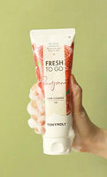 Hand holding a creamy foam-covered tube of gentle pomegranate foam cleanser against pale green background