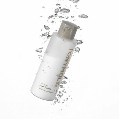 Matte white cleanser bottle with gold cap surrounded by water droplets emphasizing gentle exfoliation effect
