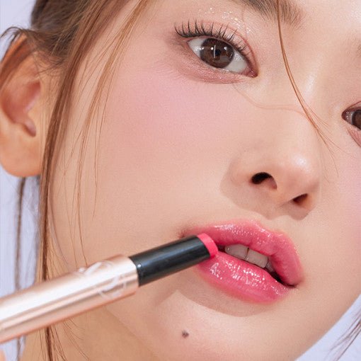 Close-up of model applying glossy pink tint balm to lips showcasing smooth, radiant finish and natural lip enhancement