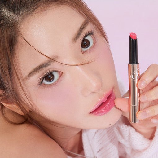 Young woman with glossy pink lips holding a sleek tinted balm stick against soft pink background