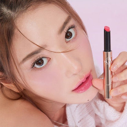 Young woman with glossy pink lips holding a sleek tinted balm stick against soft pink background