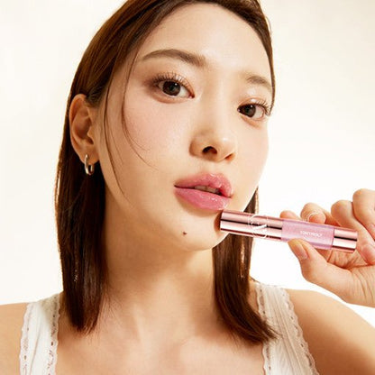 Woman applying pink lip tint in rose gold tube showcasing instant plump effect on natural lips with soft lighting