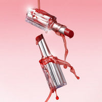 Red tinted lip balm with clear glossy casing and syrup-like liquid dripping against pink background