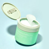 Open mint green jar with round white soothing pads lifting out, designed for calming skincare application