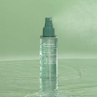 Green spray bottle of soothing mist serum standing on reflective water surface with botanical design elements