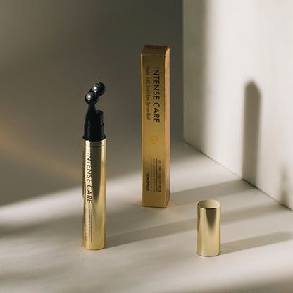 Gold tube of eye serum ball with rounded applicator beside matching box and cap in soft natural lighting