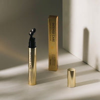 Golden tube of eye serum with black applicator featuring dual roller balls and matching gold cap on light background