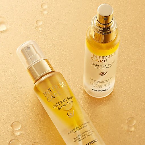 Two gold-toned serum mist bottles with pump tops on a wet gold surface showcasing deep hydration benefits