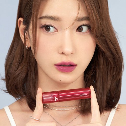 Young woman with smooth skin holding a shiny red lip product promoting long-lasting color finish