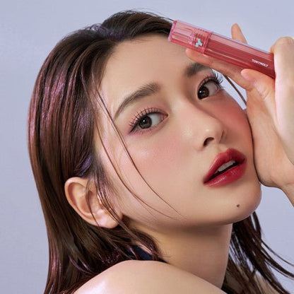 Close-up of a woman with smooth skin and bold lip color holding a red tinted lip product near her forehead