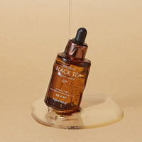 Amber glass dropper bottle with nourishing black tea oil pouring onto beige surface highlighting antioxidant benefits