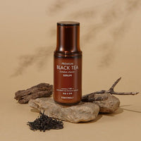 Brown bottle of moisturizing serum with black tea extract placed on natural stones with dried tea leaves nearby