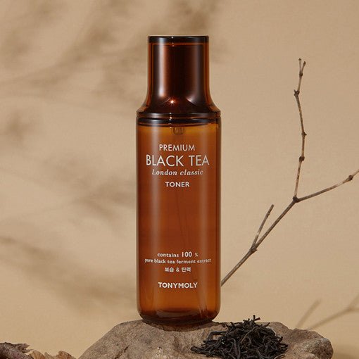 Amber bottle of moisturizing toner featuring black tea extract, placed on stone with dry branch and tea leaves backdrop