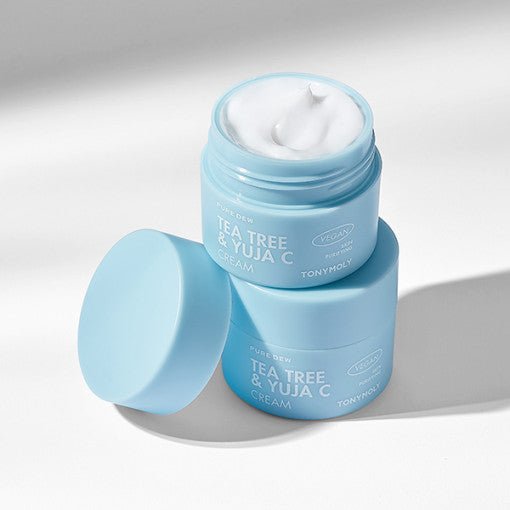 Light blue jars of hydrating tea tree and yuja cream with smooth white texture inside on white surface