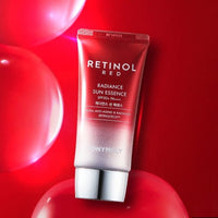 Red tube of retinol radiance sun essence with silver cap against vibrant red background with glossy spheres