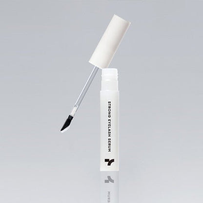 Open white bottle of eyelash serum with angled applicator brush against plain gray background
