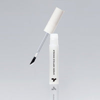 White tube of eyelash serum with angled brush applicator and black serum visible on brush tip on gray background