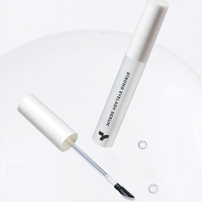 Minimalist white tube of eyelash serum with applicator brush and clear serum droplets on a smooth white surface