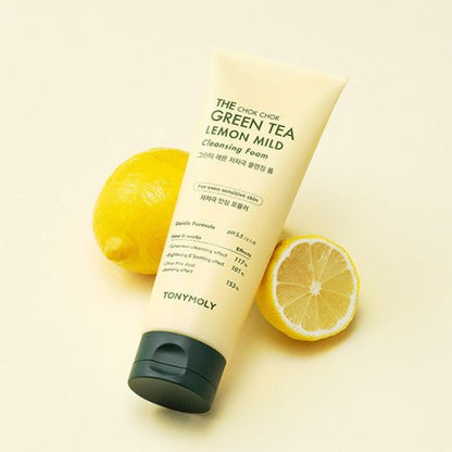 Tube of mild green tea lemon cleansing foam with black cap alongside whole and halved fresh lemons on pale background