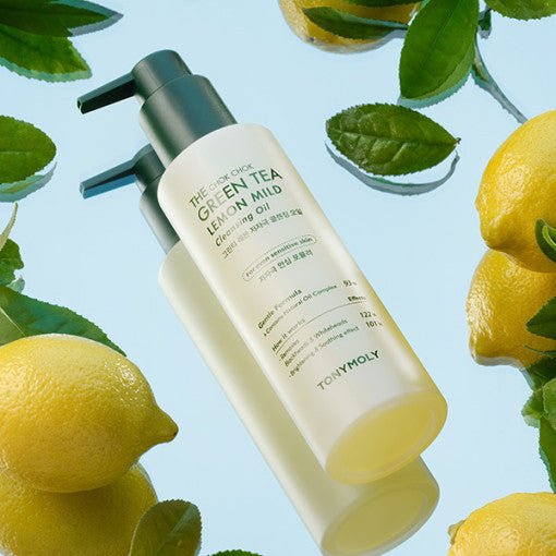Pump bottle of mild cleansing oil with green tea and lemon placed among fresh lemons and green leaves on blue surface