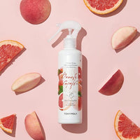 White spray bottle of gentle body peeling mist surrounded by fresh peach and grapefruit slices on pink surface