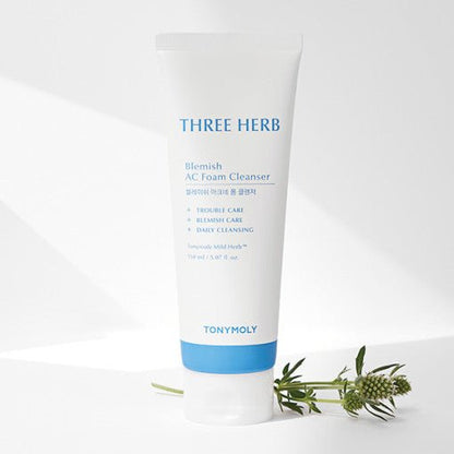 White tube of blemish foam cleanser with blue accents standing beside fresh green herb sprigs on white surface