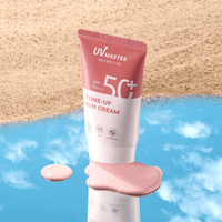 Pink and white tube of tone-up sun cream with SPF50+ PA+++ on reflective surface with sandy background and spilled cream