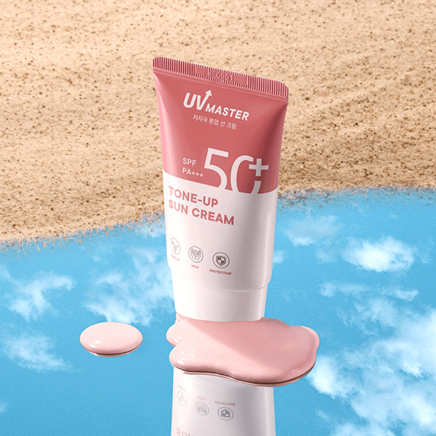 Pink and white tube of tone-up sun cream with SPF50+ PA+++ on reflective surface with sandy background and spilled cream