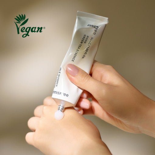 Hand applying smooth green tea essence hand cream from a white tube marked vegan for deep hydration benefits
