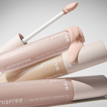 Three tubes of light fitting concealer in soft neutral shades with one applicator showing creamy texture spill